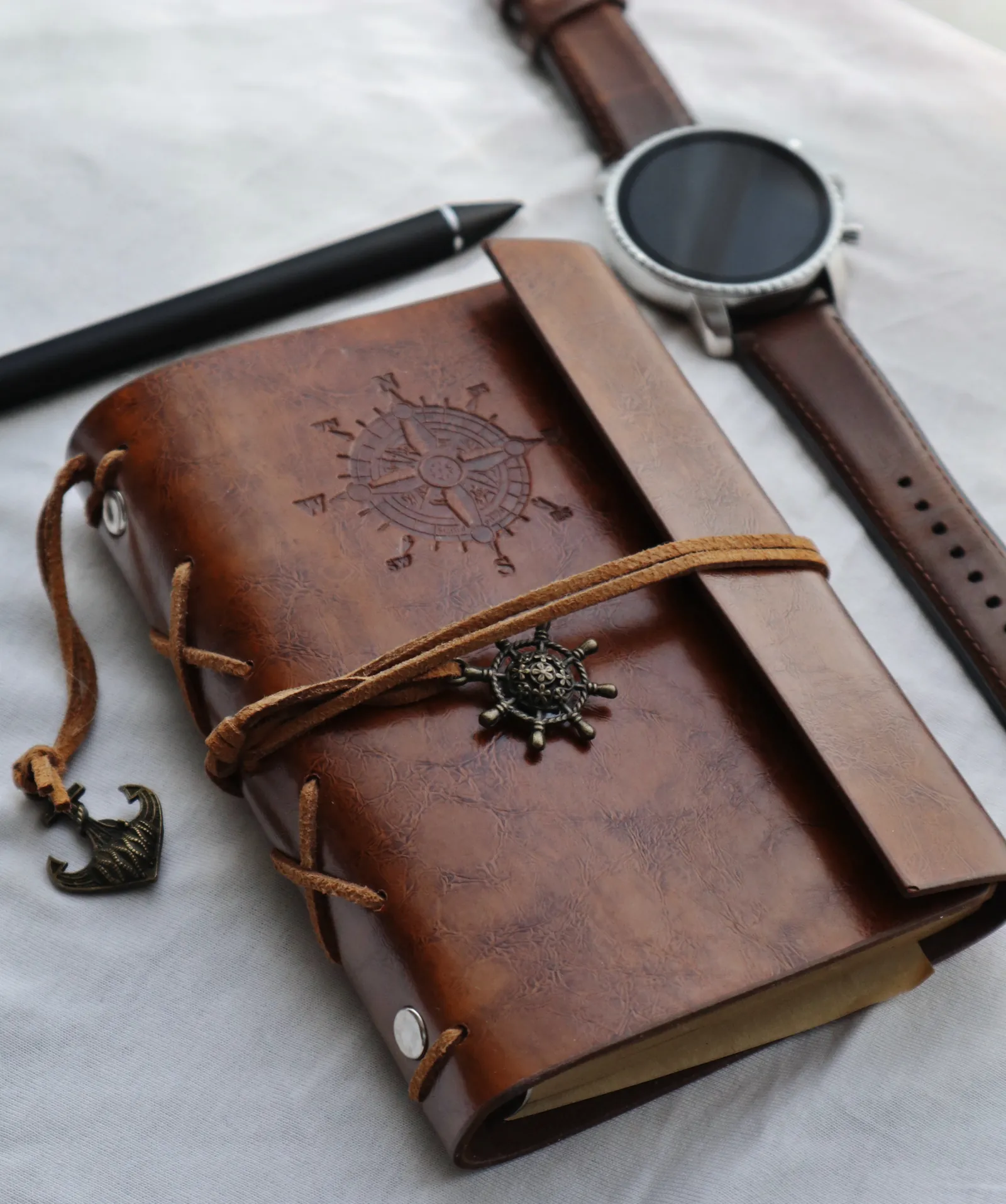 A leather travel journal with a compass emblem, beside a watch